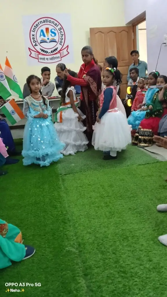 Best school in manigachhi, Indrathair and Darbhanga: Young students actively participating in a cultural celebration on a beautifully set stage at Apex International School. This top cbse school in Indrathair, Manigachhi & Darbhanga fosters confidence, creativity, and public speaking skills from an early age by integrating vibrant extra-curricular events, annual day performances, and traditional festivals into its core academic timeline.The image captures elementary-aged girls dressed elegantly in colorful white and flowing blue princess gowns, performing on an artificial green grass carpet stage while guided closely by their supportive teachers. In the background, the official "AIS" Apex International School crest banner is displayed prominently alongside multiple Indian national flags, highlighting a strong focus on patriotic values and school community pride.As a leading top school in Indrathair, Manigachhi & Darbhanga, the campus provides a premium, well-rounded learning environment that blends high international education standards with cultural refinement. This continuous emphasis on creative stage expression makes it the best english school in manigachhi, Indrathair and Darbhanga for parents seeking overall personality development and student excellence. By building leadership qualities early on, this premier top english school in Indrathair, Manigachhi & Darbhanga prepares its young scholars for future milestones in a supportive, lively community.
